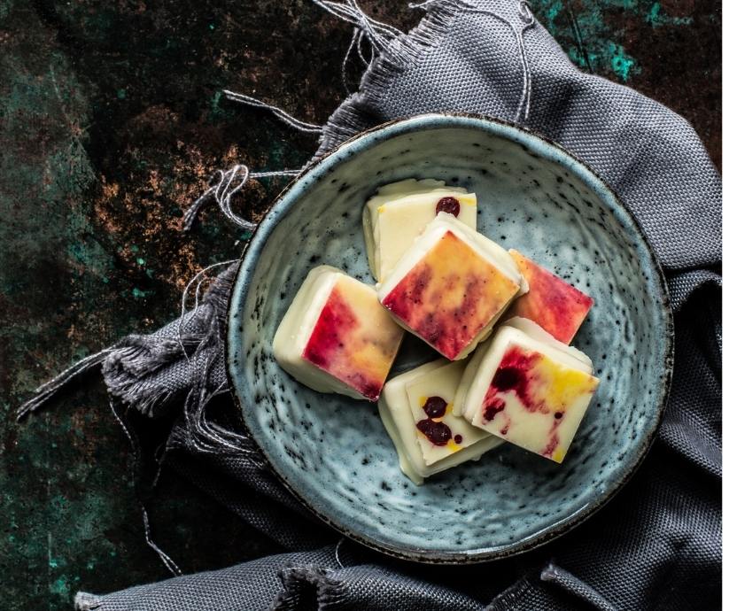 Handgemachte Arancia-Praline mit Mandelnougat, Orangenkeks und farbigen Plättchen in Gelb-Rot-Orange auf Keramikteller