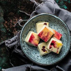 Handgemachte Arancia-Praline mit Mandelnougat, Orangenkeks und farbigen Plättchen in Gelb-Rot-Orange auf Keramikteller
